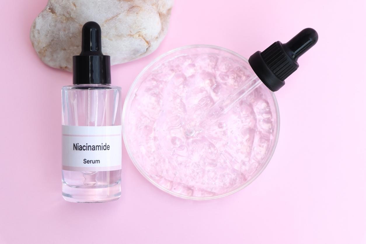 Niacinamide contre l'acné : flacon avec pipette sur fond rose