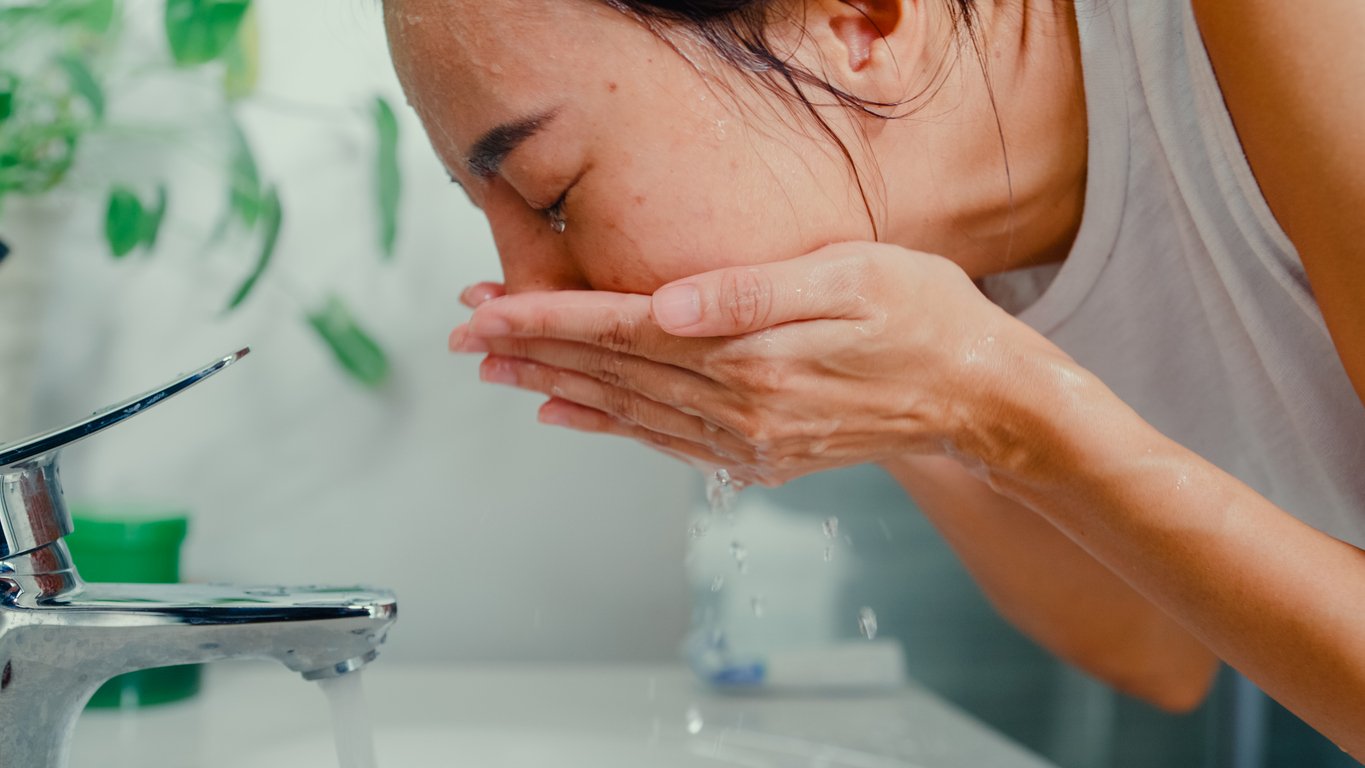 Peeling bei Akne: Junge Frau wäscht ihr Gesicht über dem Waschbecken