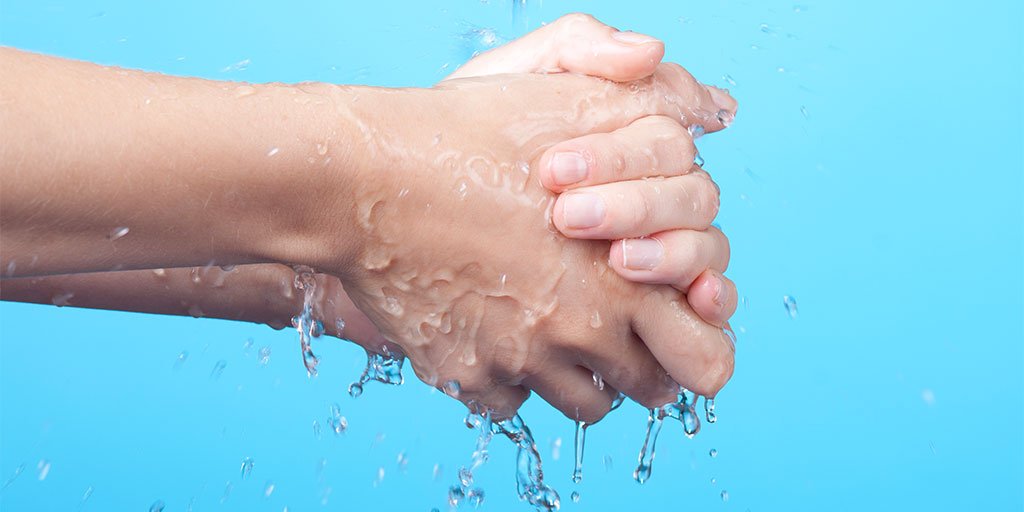 Hände, die sich unter einem fließenden Wasserstrahl waschen, vor einem hellblauen Hintergrund