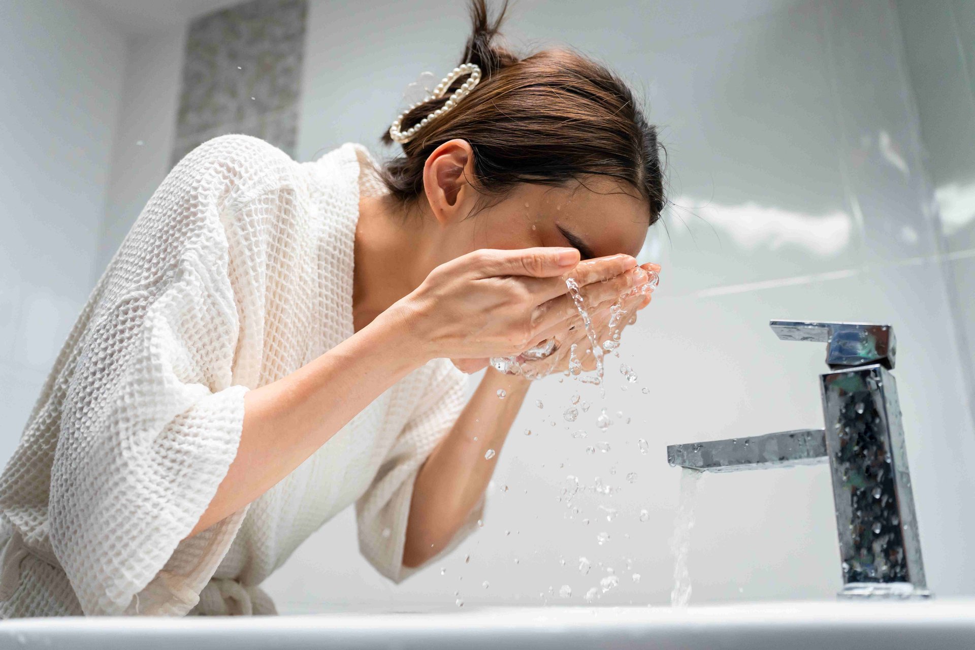une femme se lave le visage à l'eau claire au lavabo.