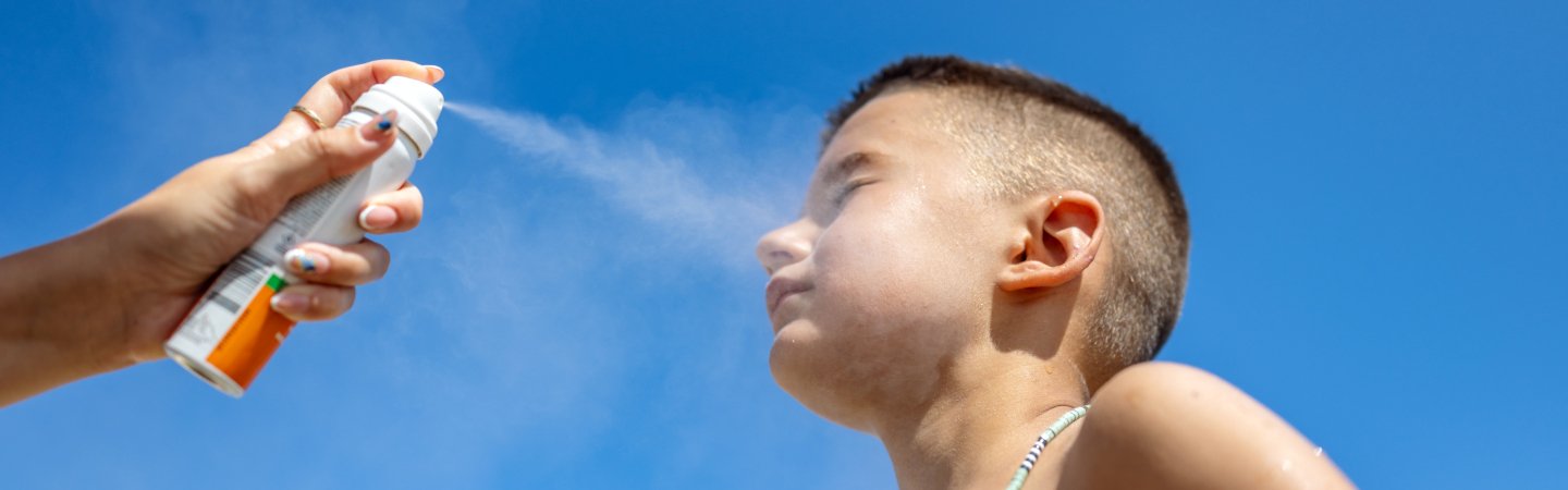 Auftragen eines Sonnensprays auf die Haut im Freien unter blauem Himmel.