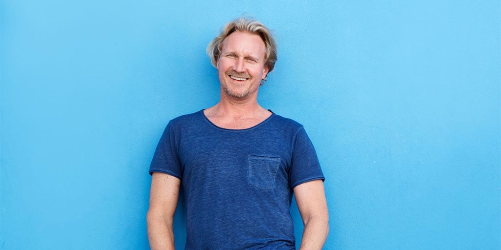 Lächelnder Mann in einem dunkelblauen T-Shirt vor hellblauem Hintergrund