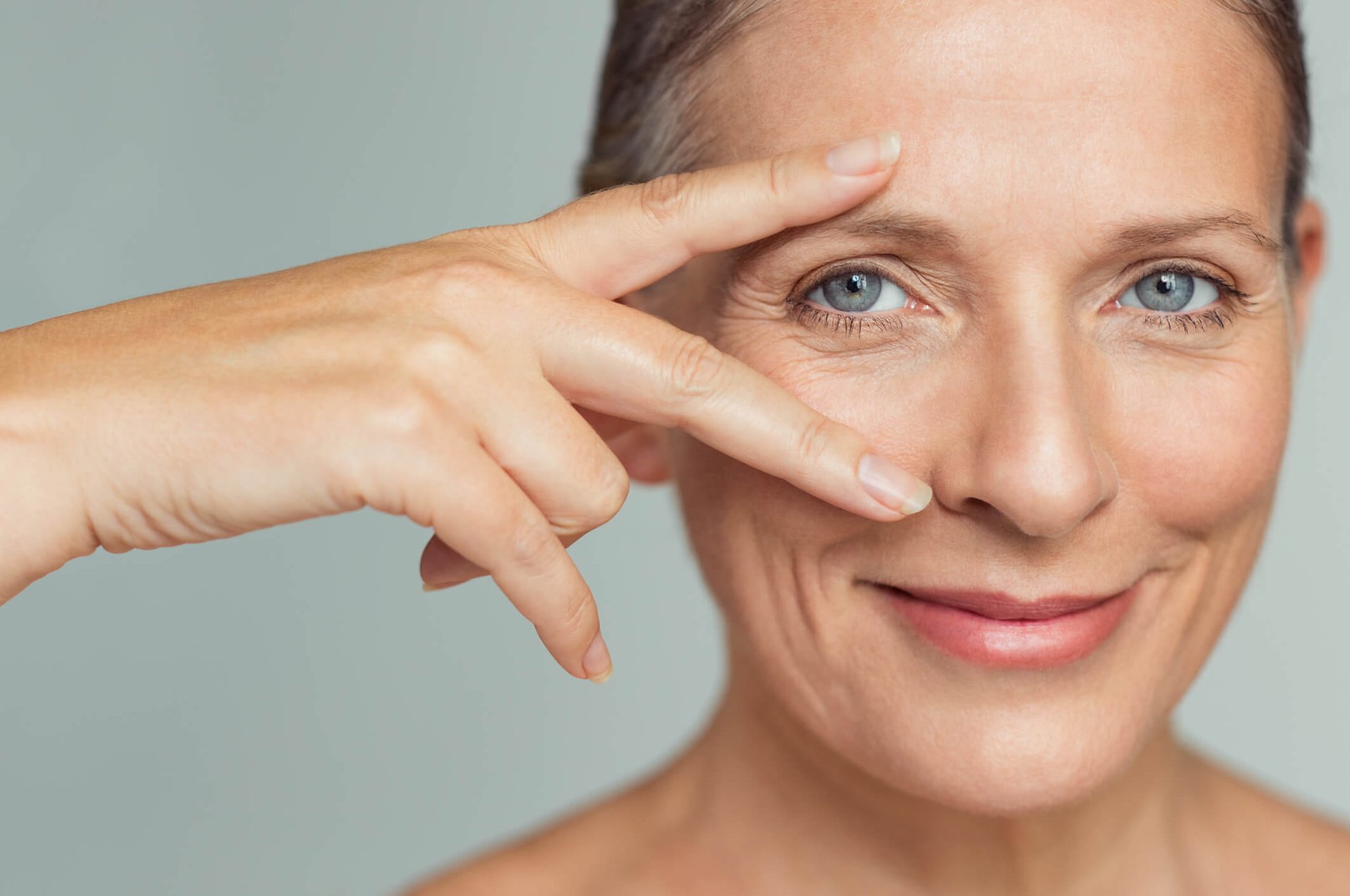 Femme avec de légères rides autour des yeux pose deux doigts sur son visage.