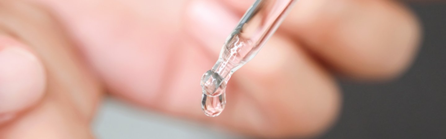 Ein Tropfen eines Hyaluronsäure-Serums tropft aus einer Pipette auf einen Finger 
