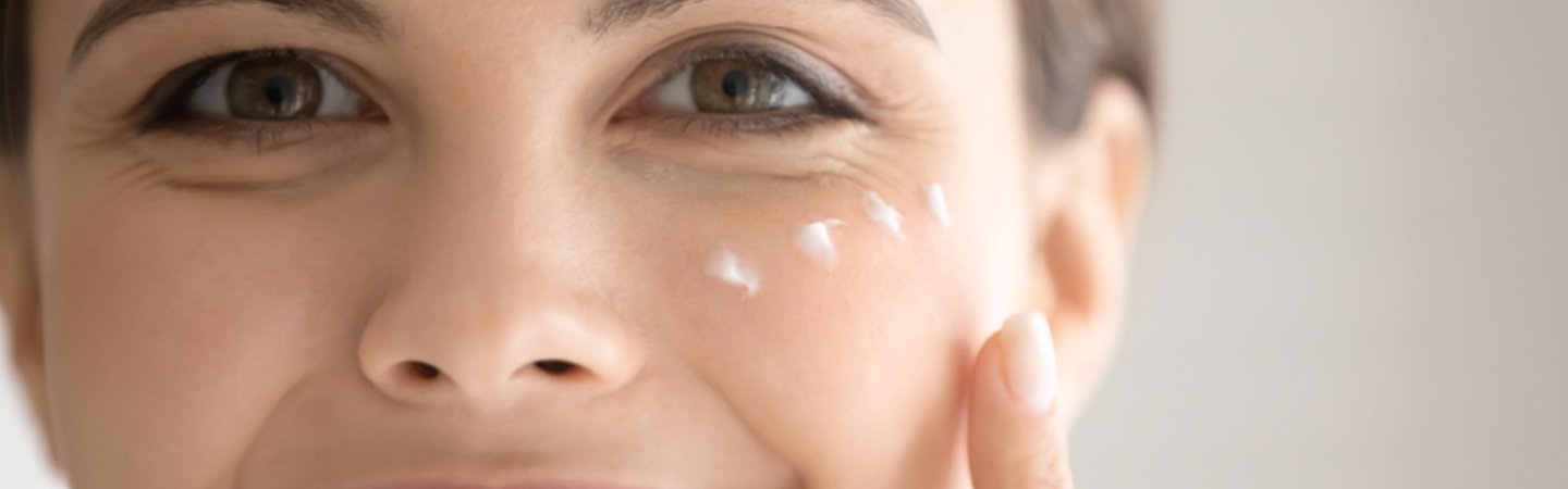 Augenpartie einer Frau mit Fältchen und Creme-Tupfen um die Augen