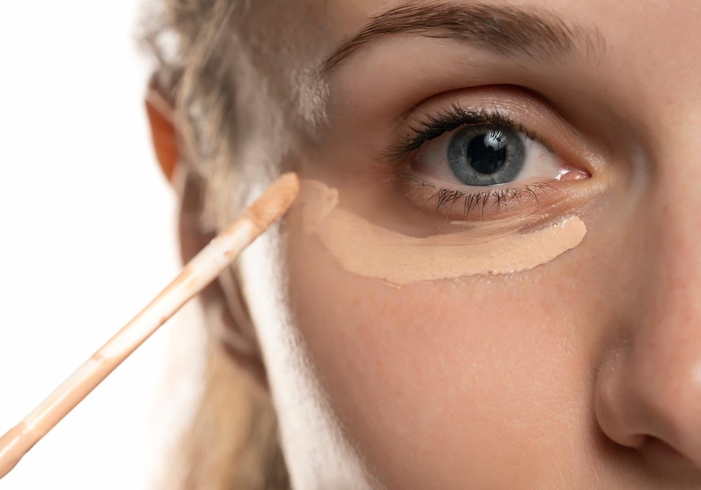 Frau trägt Concealer unter den Augen auf, um Augenringe abzudecken