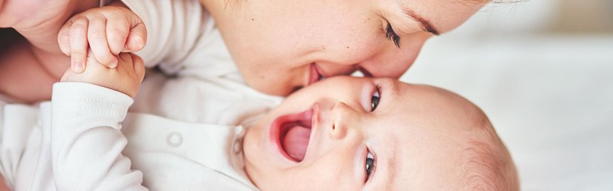 Une mère embrasse son bébé souriant sur la joue.