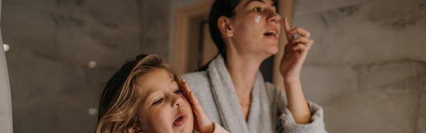 Maman et sa fille appliquent de la crème sur leur visage dans la salle de bain devant le miroir.