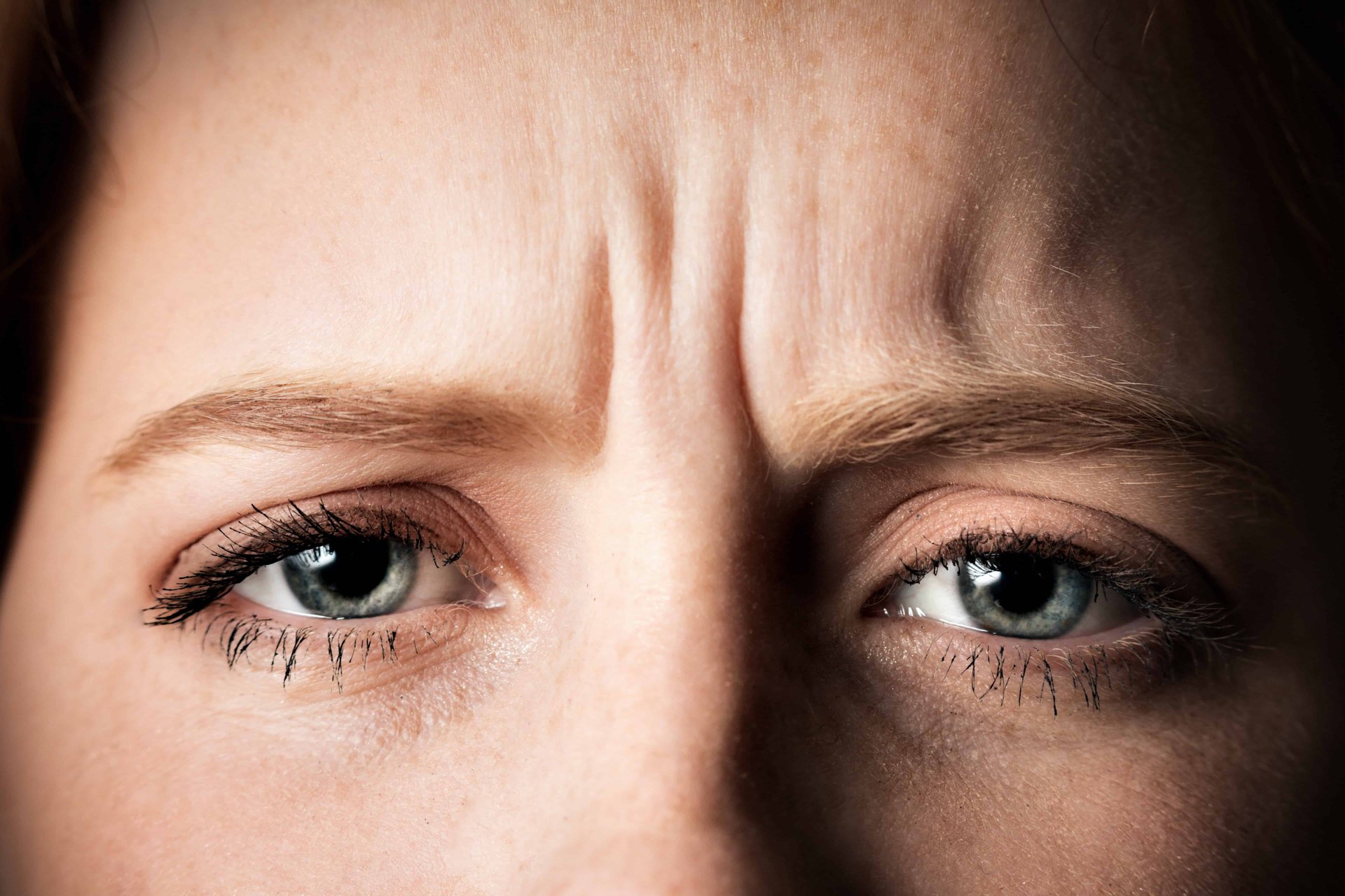 Nahaufnahme eines besorgten Gesichtsausdrucks mit Zornesfalte und blauen Augen