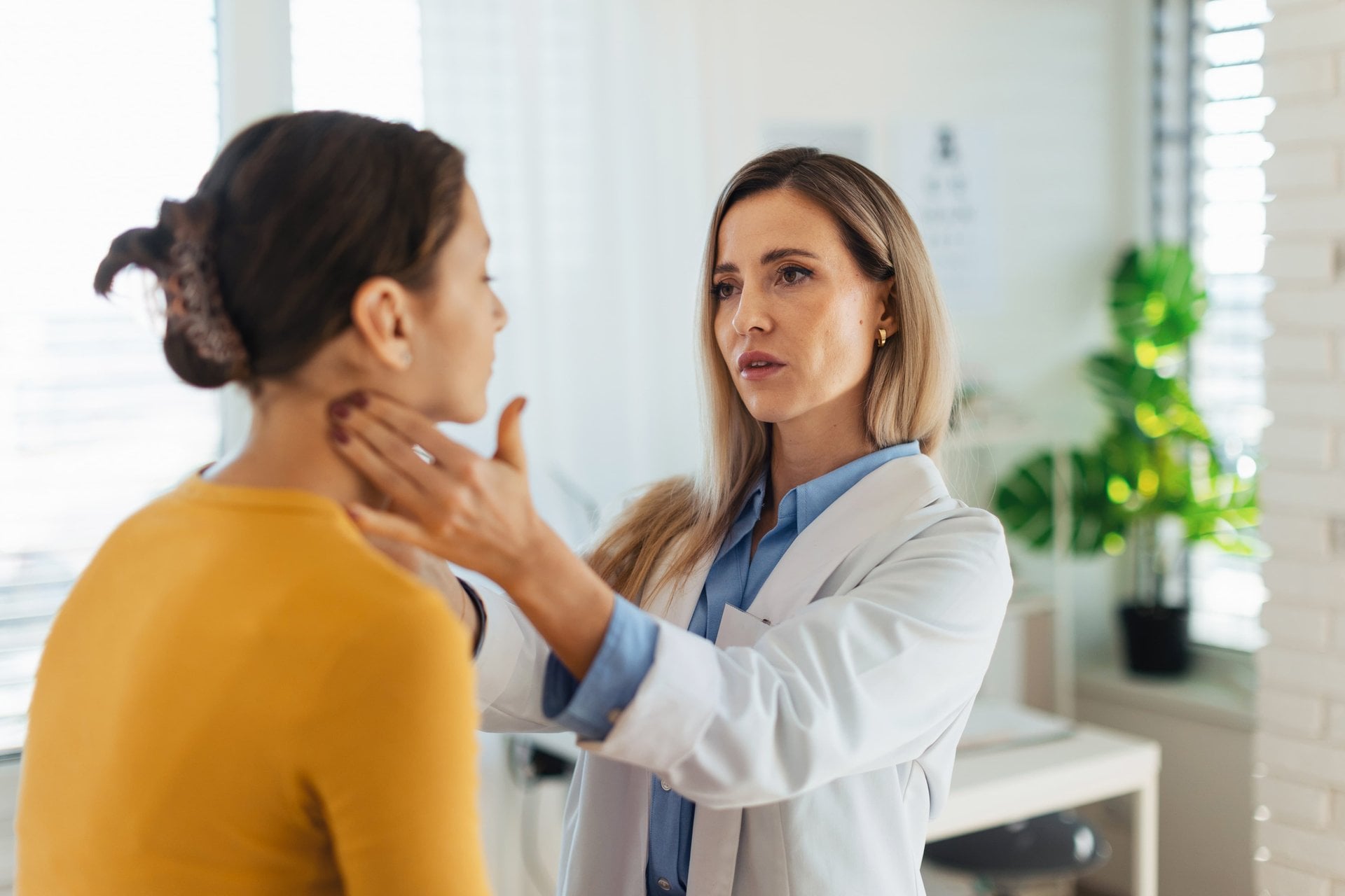 Ärztin untersucht den Hals einer Patientin in einer hellen Praxis
