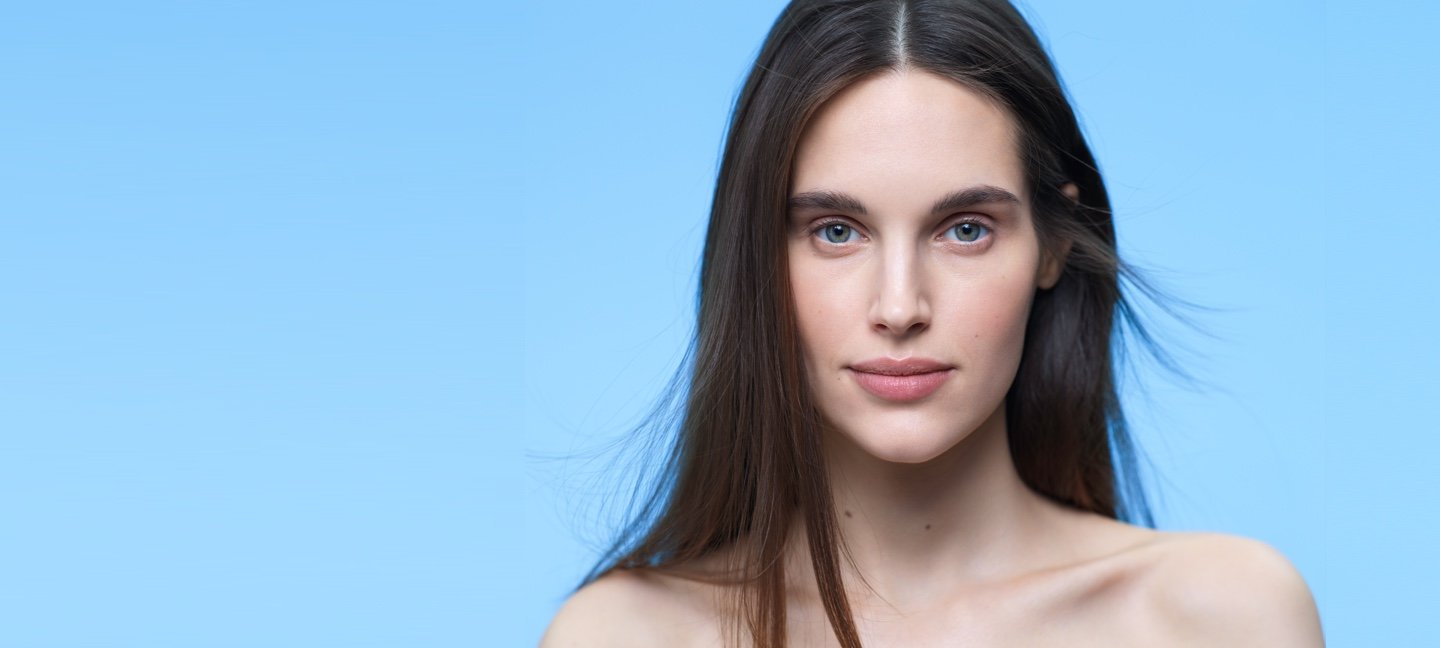 Une femme aux cheveux bruns devant un fond bleu clair