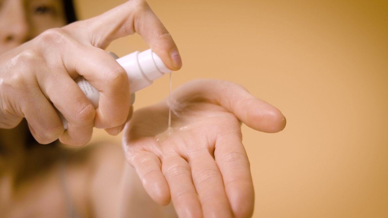 Deux mains visibles sur fond jaune : une main applique du gel sur l'autre en pressant un flacon