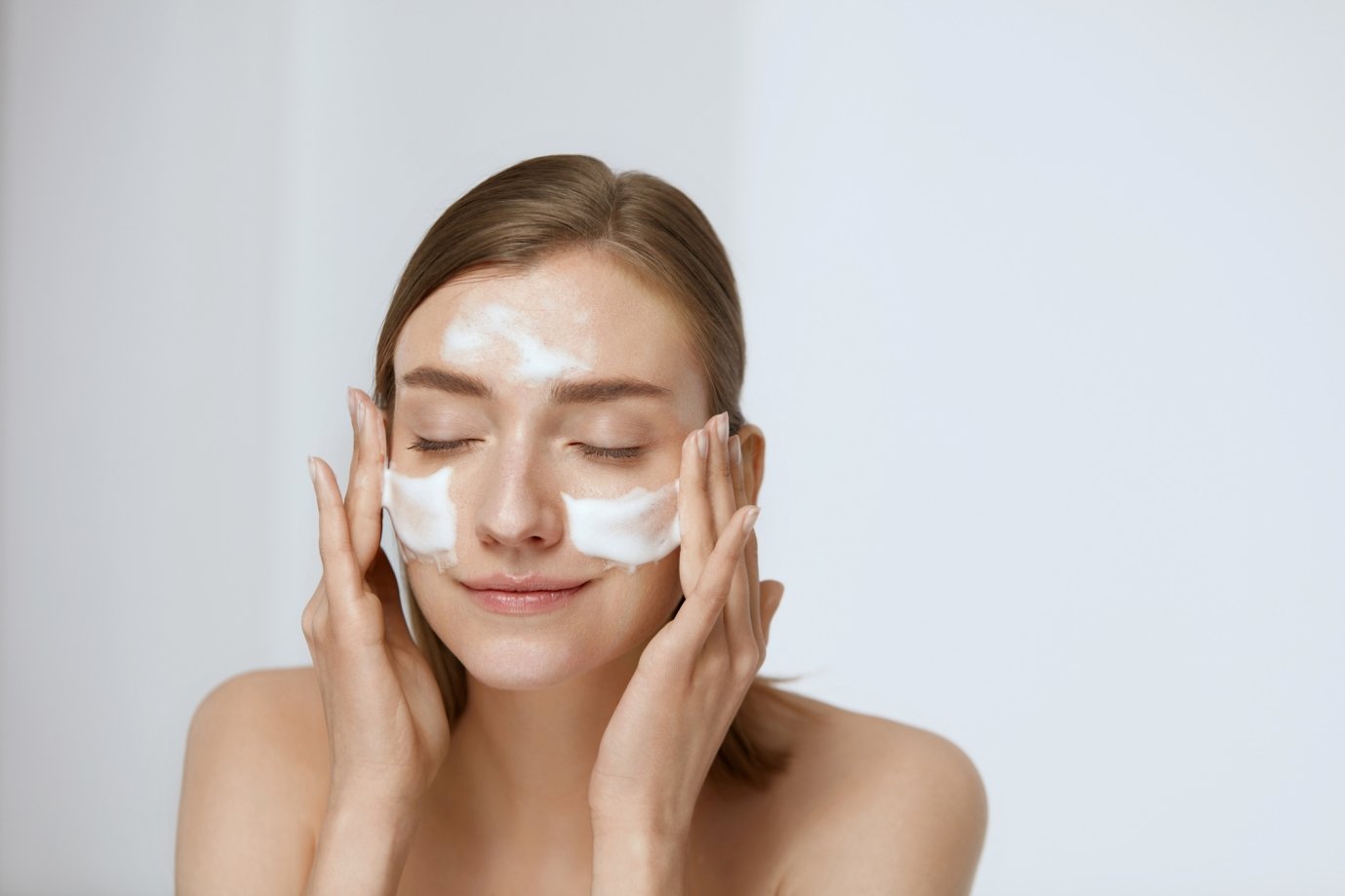 Une femme fait mousser un nettoyant visage sur ses joues et son front
