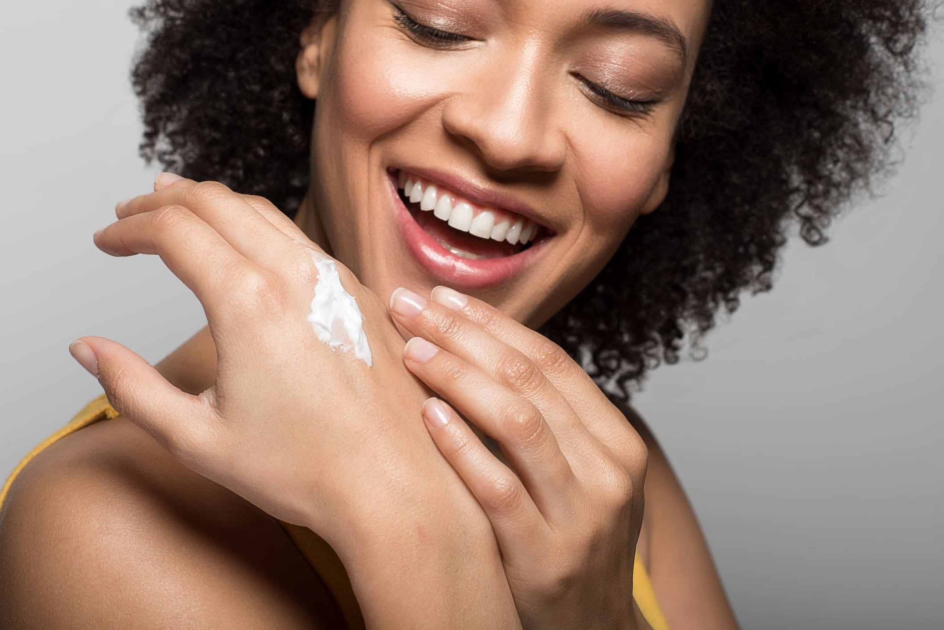Junge Frau mit dunklem, lockigem Haar cremt ihre Hände mit Sheabutter-Handcreme ein