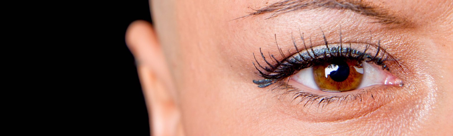 Gros plan d'un œil humain avec des cils détaillés et une iris brune sur fond noir.