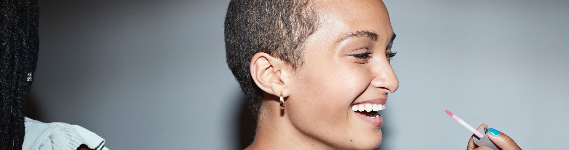 Gros plan d'une femme souriante aux cheveux très courts qui applique du gloss.