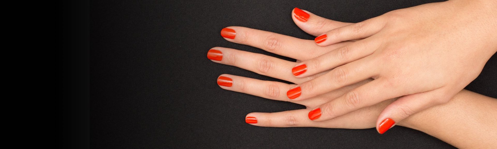Mains avec une manucure discrète et un vernis à ongles rouge vif sur fond noir.