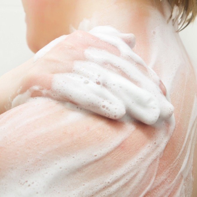 Person wäscht sich die Schulter mit schäumendem Duschgel, Nahaufnahme der Haut.