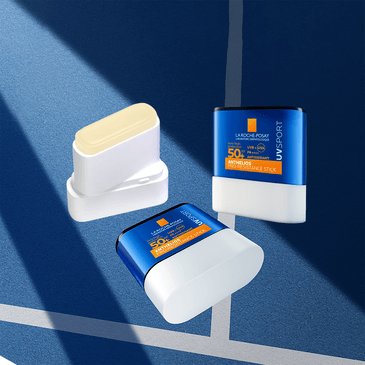 Drei Anthelios PRO SPORT Stick LSF 50+ in offener und geschlossener Form auf blauem Untergrund mit tennisplatzartiger Linie.