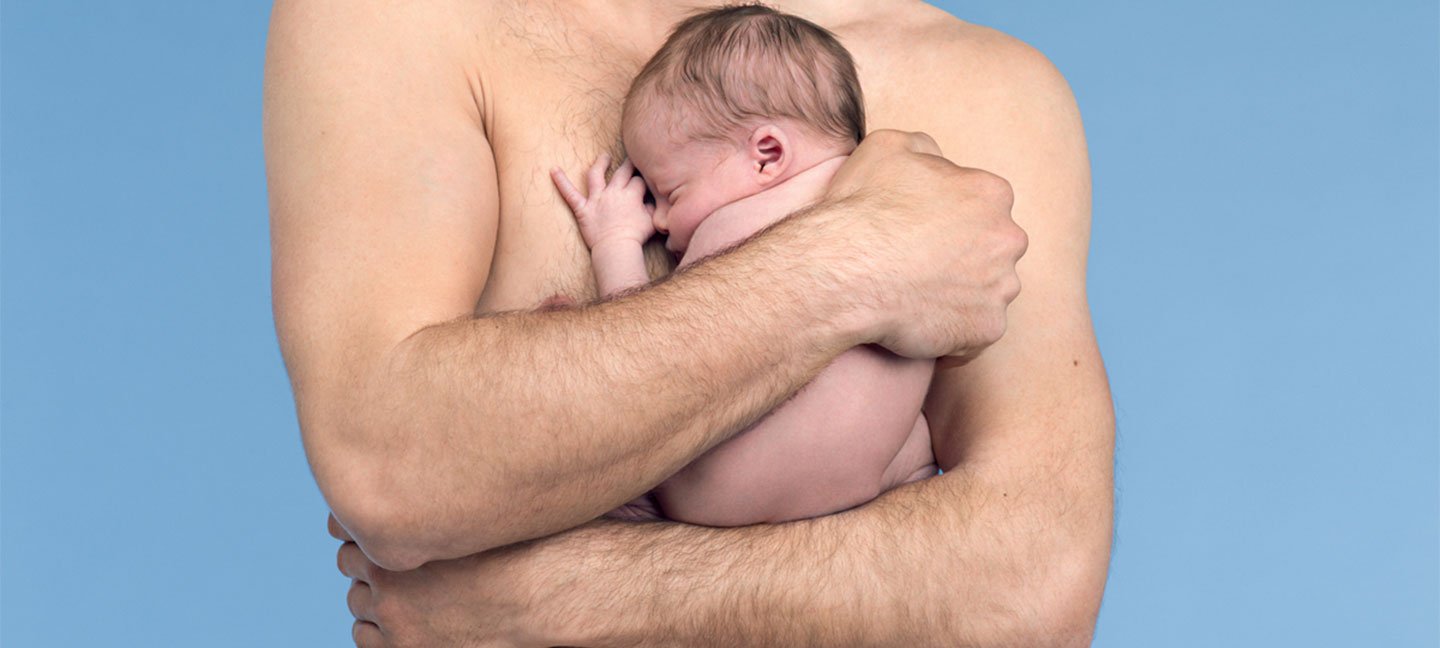 Ausschnitt von einem Mann vor hellblauem Hintergrund, der ein Baby in den Armen hält
