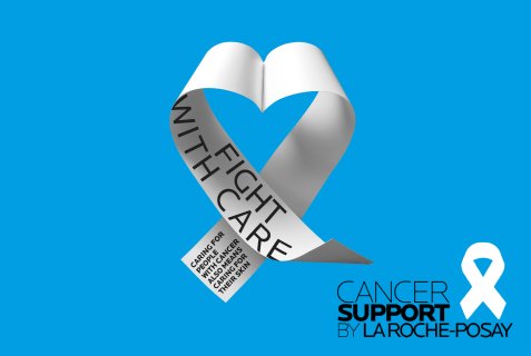Ruban argenté en forme de cœur avec l'inscription « Fight With Care » sur fond bleu, symbole de la prévention du cancer, accompagné du logo « Cancer Support by La Roche-Peyre ».