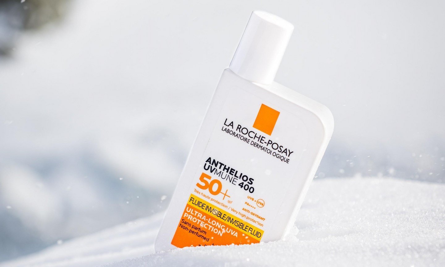 Eine Flasche eines ANTHELIOS Sonnenprodukts mit LSF 50+ steckt leicht schräg im Schnee.