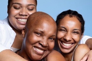 Trois femmes sourient et se prennent dans les bras sur un fond bleu